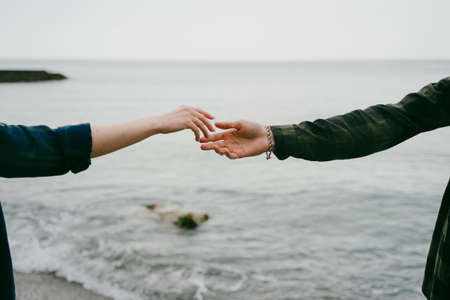 The hand of a girl and a guy reach out to each other on the seashore.の写真素材