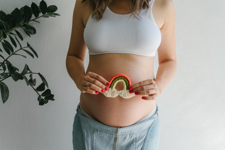 A pregnant girl in a denim jumpsuit holds a rainbow in her hands for the decor of a childrens room.の写真素材