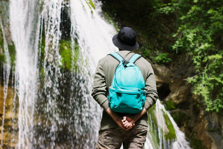 A guy with a blue backpack on his back looks at the waterfall.の写真素材