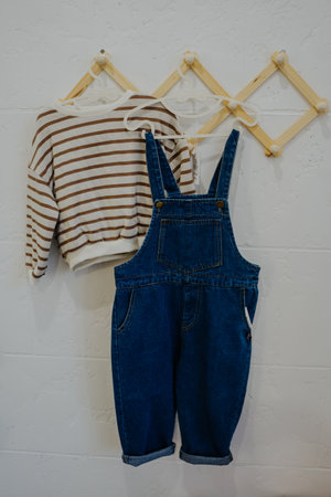 Fashionable childrens clothes hanging on a wooden hanger. Denim overalls and striped sweater.の写真素材