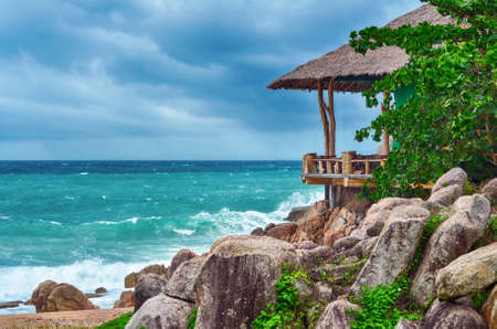 Bamboo bungalow at the rocky cliff and stormy sea and skyの写真素材