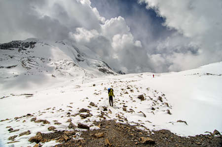 Trekkers climb down from the pass through snowy mountains under stunning cloudy skyの写真素材