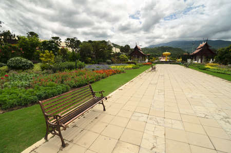 View to the path with few benches through the garden featuring traditional Thai temples, flowers and monumentsの写真素材