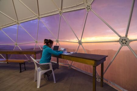 Scientist with his paper work in a dome tent sitting in front of window and stunning sunset skyの写真素材