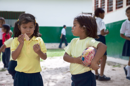 CANAIMA, VENEZUELA, 11 NOVEMBER 2010: Pemon girl with a ball looking at girl with wafer at shchool yardのeditorial素材