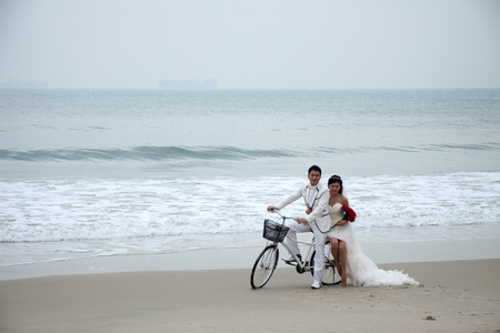 SHENZHEN, CHINA, 2011-11-26: Chinese couple posing for wedding photoshoot at the beach on a bicycleのeditorial素材