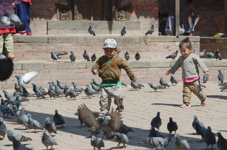 KATHMANDU, NEPAL, 2013-02-26: little kids startles numerous pigeons at the ancient squareのeditorial素材