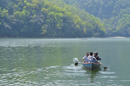 POKHARA, NEPAL, 2013-04-02: three men sailing in small fisherman boat on a lakeのeditorial素材