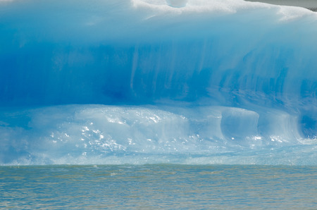 Closeup view of an icebers, glowing on the sun blue ice and some lake water beneath it. Beautiful...