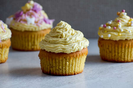 Four frosted yellow cupcakes with sprinkles and grey textured background