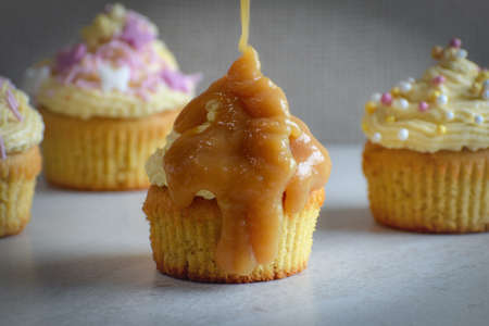 Four frosted cupcakes with butterscotch sauce drizzling over topの写真素材