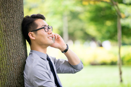 Young asian businessman using tablet, mobile phone in the parkの写真素材