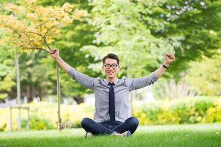 Young asian businessman using tablet, mobile phone in the parkの写真素材
