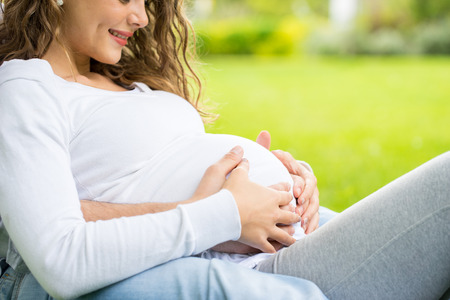 Happy and young pregnant couple in park in summer