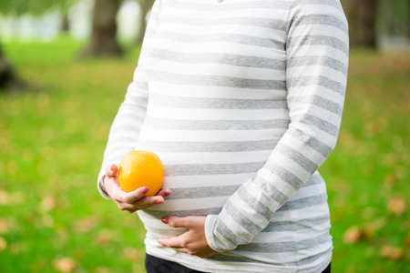 Happy and young pregnant woman with food in the parkの写真素材