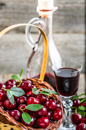 Glass of liquor with cherry fruits and rustic bottle, homemade alcohol tincture on wooden tableの写真素材