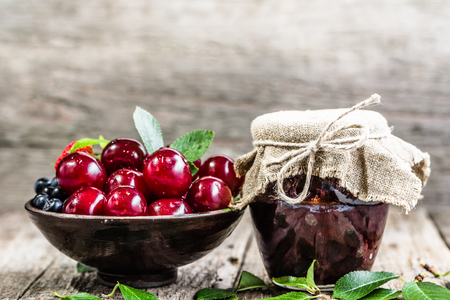 Rustic jar with homemade cherry jam and fresh cherries in a bowlの写真素材