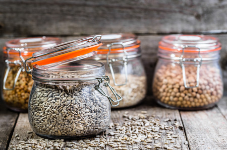 Healthy vegan food, seeds and grains in jars on rustic table, chickpeas, peas, sunflower seed, oatmealの写真素材