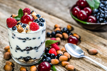 Cold yogurt ice cream with berry fruits and hazelnuts in a glass cup, frozen dessert, summer healthy breakfast conceptの写真素材