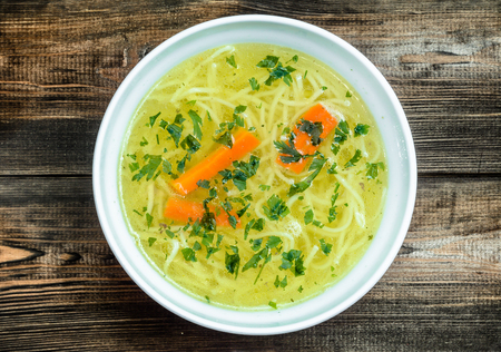 Chicken broth soup with noodles on a wooden table.の写真素材