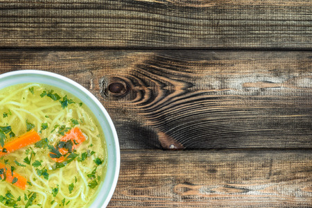 Chicken broth soup with noodles on a wooden table.の写真素材