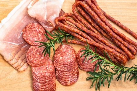Assortment of meats: kabanos, salami prosciutto slices on wooden board.の写真素材
