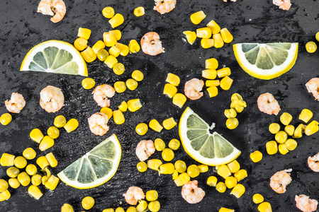 Colorful vegetable or mediterranean cuisine background with shrimps, corn and lemon slices on black plate, flat layの写真素材