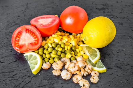 Colorful vegetable and fruit background with shrimps, tomato, corn and lemon on black plateの写真素材