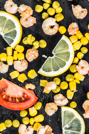 Colorful vegetable or mediterranean cuisine background with shrimps, tomato, corn and lemon slices on black plate, flat layの写真素材