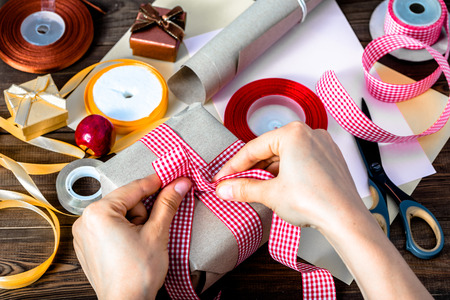 Wrapping christmas present with gray paper and ribbons. Hands making bow on gift, rustic styleの写真素材