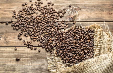 Black coffee beans in burlap sack on wooden tableの写真素材