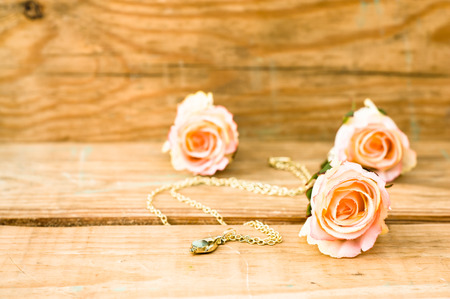 Pink roses and golden necklace on a vintage wooden backgroundの写真素材