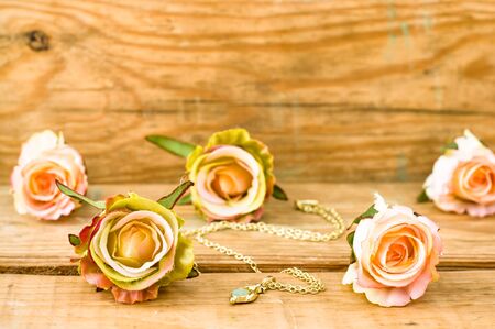 Pink roses and golden necklace on a vintage wooden backgroundの写真素材