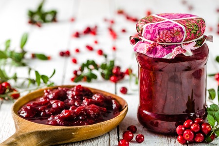 Spoon and jars of jam with cranberry on white wooden backgroundの写真素材
