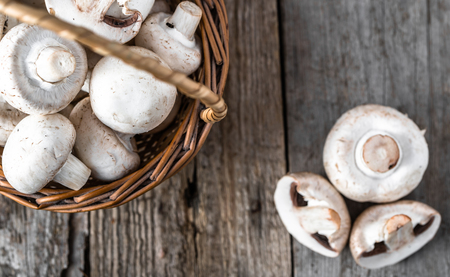 Fresh champignon mushrooms in a basket on wooden table, overheadの写真素材