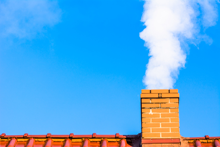 Modern house roof with chimney smoke, air pollution and smog in winter, ecological problemsの写真素材