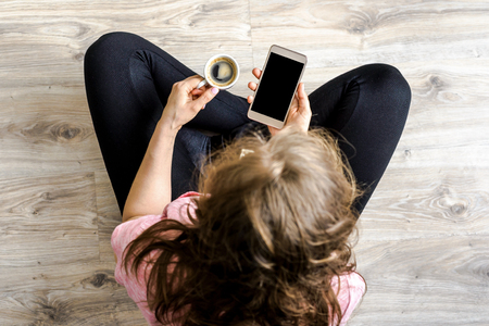Woman with smart phone in hand and coffee drinking hipster person using smartphone, top viewの写真素材
