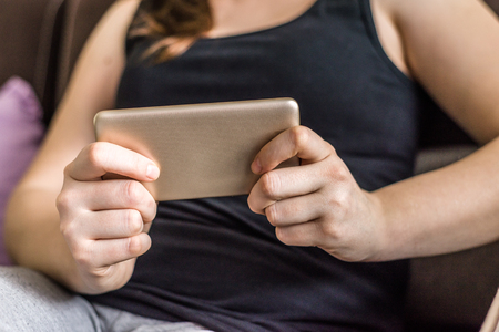 Person with mobile phone, playing games or watching movie on the smartphone, relax and cozy moment on sofa at homeの写真素材