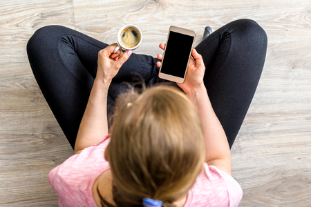 Woman using smartphone and coffee, top view, smart mobile phone used by hipster person at homeの写真素材