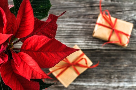 Christmas gift boxes, wrapped presents in rustic package and red poinsettia flower on wooden backgroundの写真素材