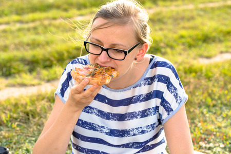 Young woman eating pizza on meadow, relax in natureの写真素材
