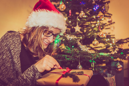 Happy christmas woman opening gift box at the xmas tree, eve at home. Winter holiday tradition.の写真素材