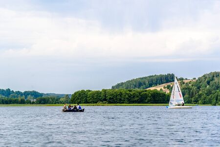 BRODNICA, POLAND - JULY 07, 2018: People on row boat and sailing yacht on the lake. Sport and summer holiday in nature. Kaszubian lake in Poland.のeditorial素材