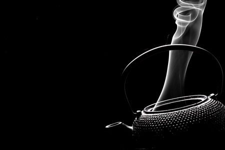Antique teapot with steaming hot tea on black background.の写真素材