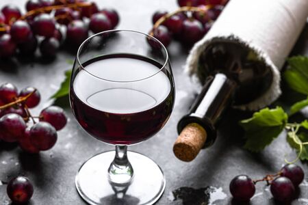 Glass of wine with red grapes and wine bottle in a cellar