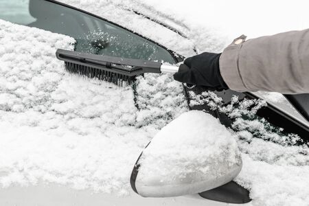 Woman cleaning car from the snow with brush. People in snowy cold weather in winter and...