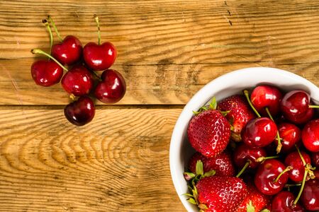Fresh fruit in a bowl on wood background. Strawberries and cherries, top viewの写真素材