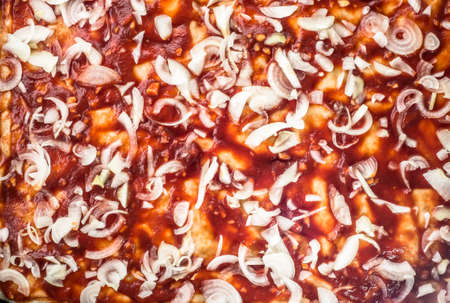 Preparation of pizza margherita with tomato sauce and raw onion sliced, top view, close-up for background or texture.の写真素材