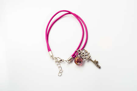 Close-up of handmade bracelet made with pink leather, crystal glass and pendant in shape key isolated on white background.の写真素材