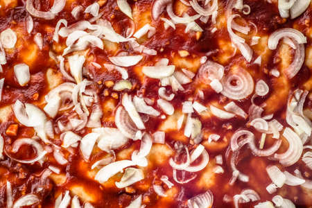 Preparation of pizza margherita with tomato sauce and raw onion sliced, top view, close-up for background or texture.の写真素材